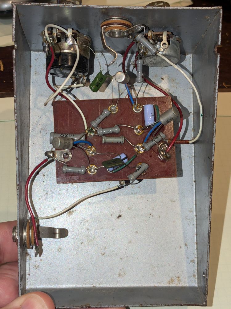 A view of the interior of a very old fuzz pedal (guitar effect), a wedge-shaped dull gray metal box with patches of rust and very old components, probably from the 1960s.