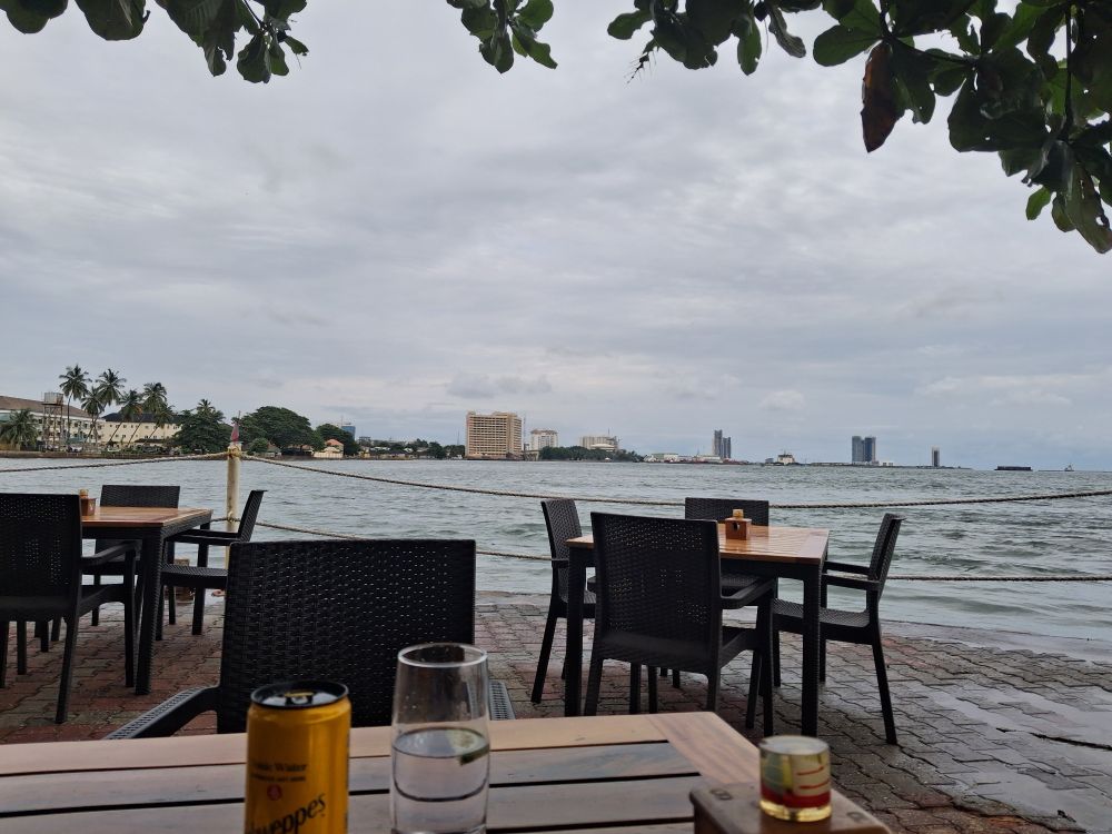 A terrace with chairs and a gin and tonic in the foreground, with a view of the Lagos lagoon and on the horizon the Lagos Island skyline.
