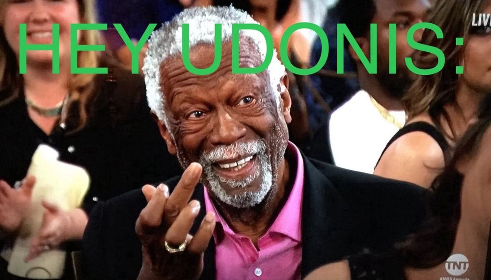 Photo of Bill Russell at an awards ceremony; he is wearing a pink button up shirt and black sport jacket while smiling and raising his middle finger.

Green text overlayed at the top of the image reads: “HEY UDONIS:”