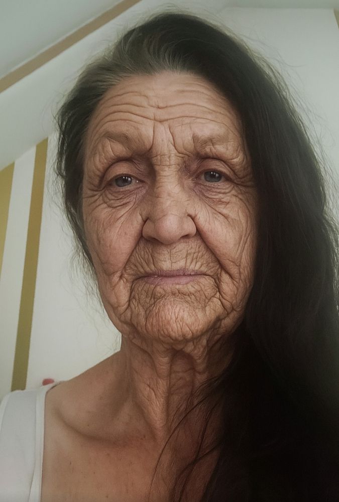 Bearbeiteten Foto der Userin. Sie hat ein sehr faltiges Gesicht, lange dunkle Haare, der Ansatz leicht gräulich. 