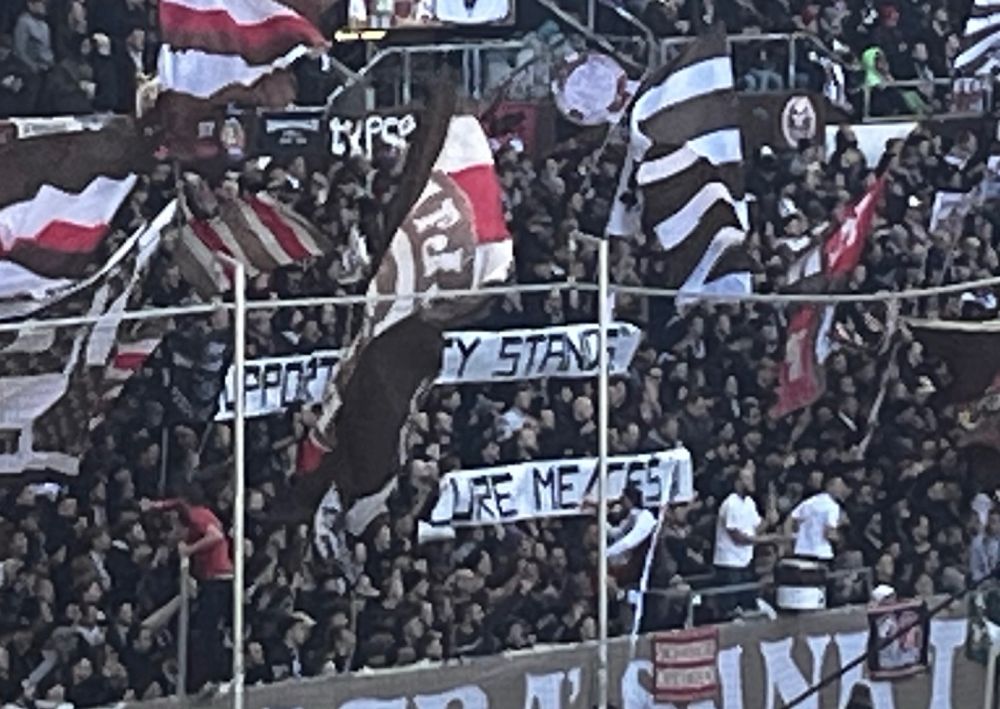 Auf zwei Tapeten in einer vollen Stehplatzkurve beim FC St. Pauli steht „Support „Empty Stands““
„Cure ME/CFS“.
Das Wort „empty“ ist auf dem Bild von einer Fahne verdeckt. 