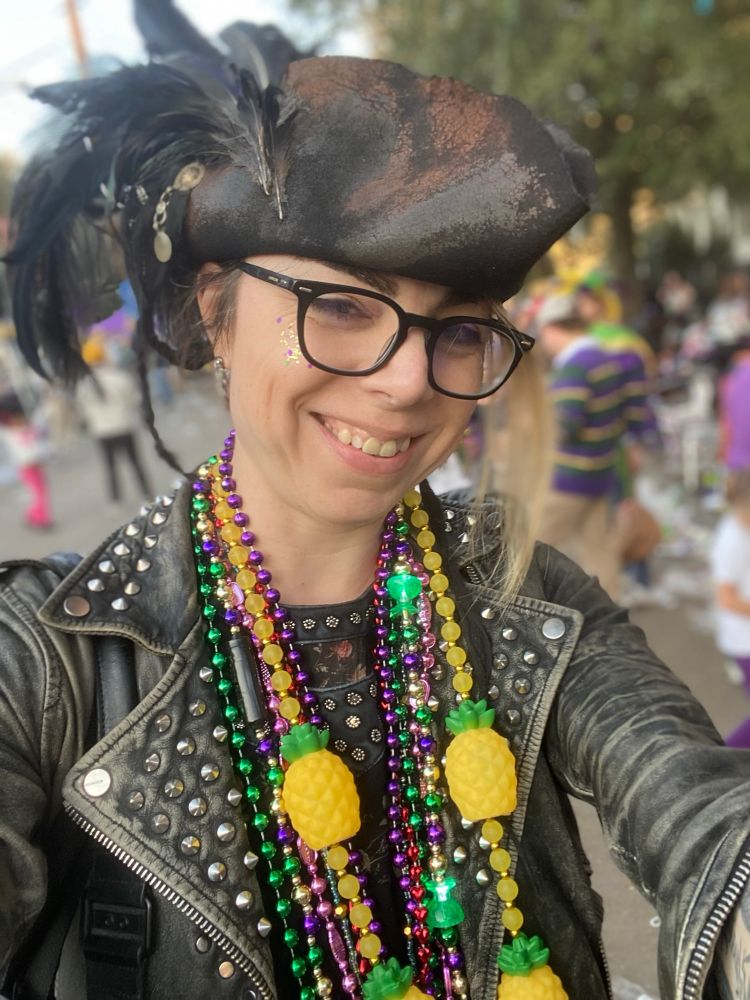 A smiling whit woman in a tricorn hat and studded leather jacket between parades on St. Charles street. 