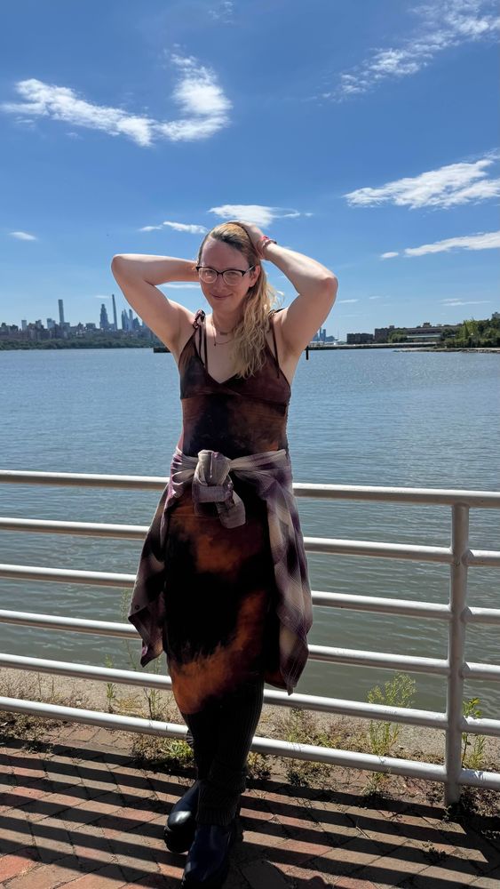 rennie adjusting her hair leaning against a railing with nyc in the background