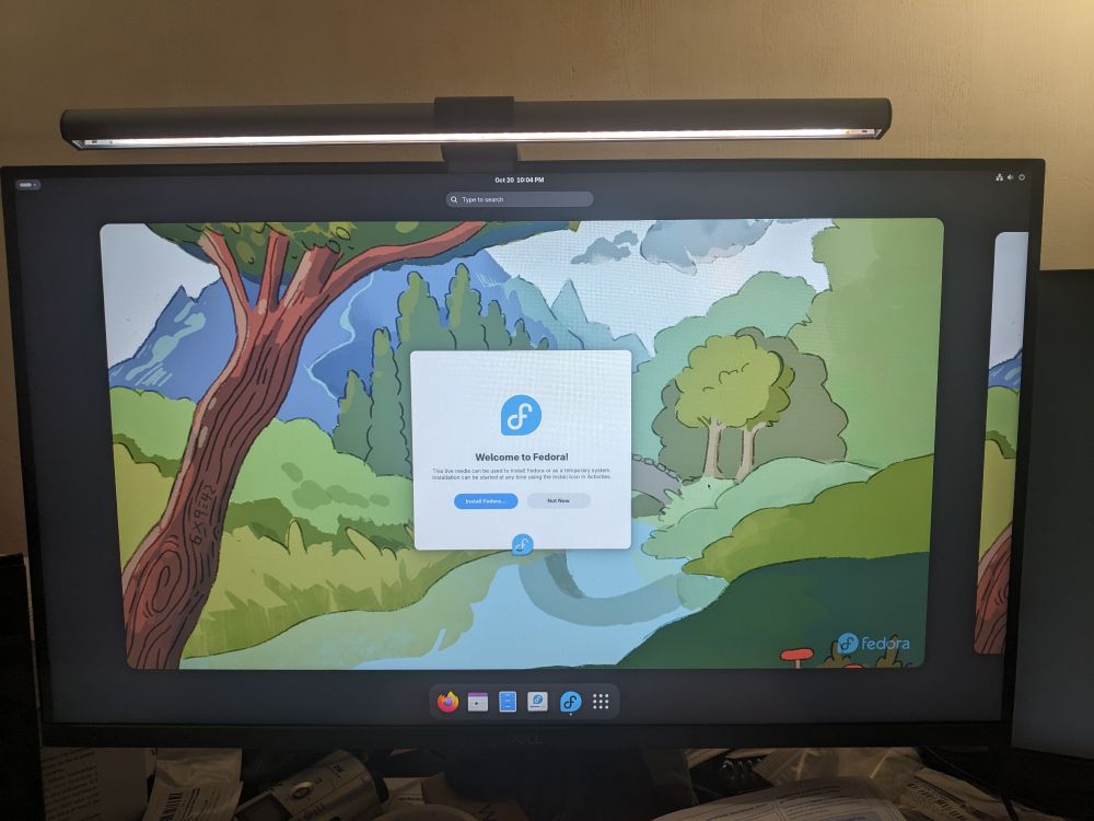 Photo of a computer screen, showing the desktop of Fedora Linux, with a window offering to begin the installation