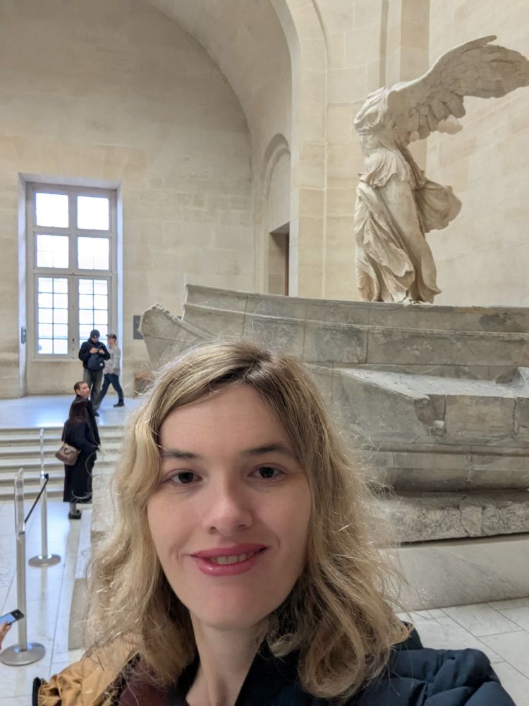 Selfie of blonde woman with Wings of Triumph statue. 