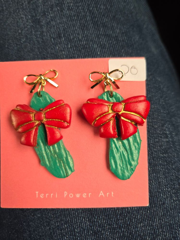 A pair of pickle earrings with a red bow around them.