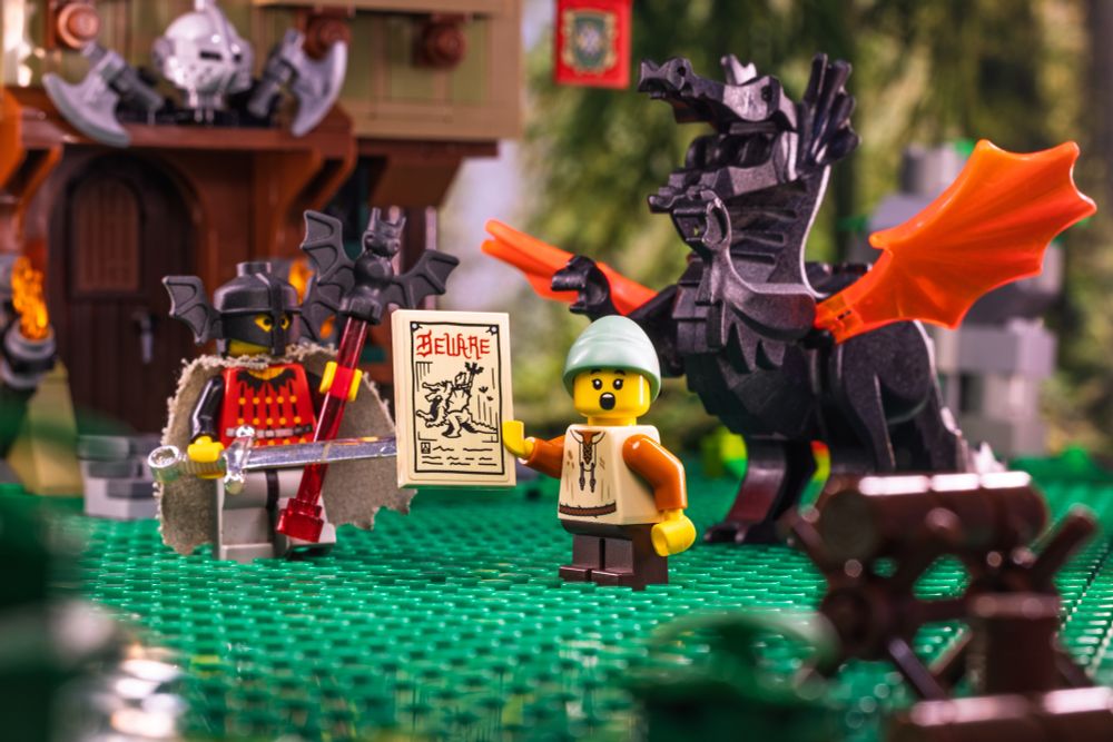 LEGO medieval village minifig lad holding the beware poster in shock as the bat lord and dragon stand behind him.