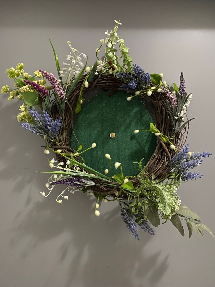 Wreath with round, green door in the center surrounded by pastel flowers