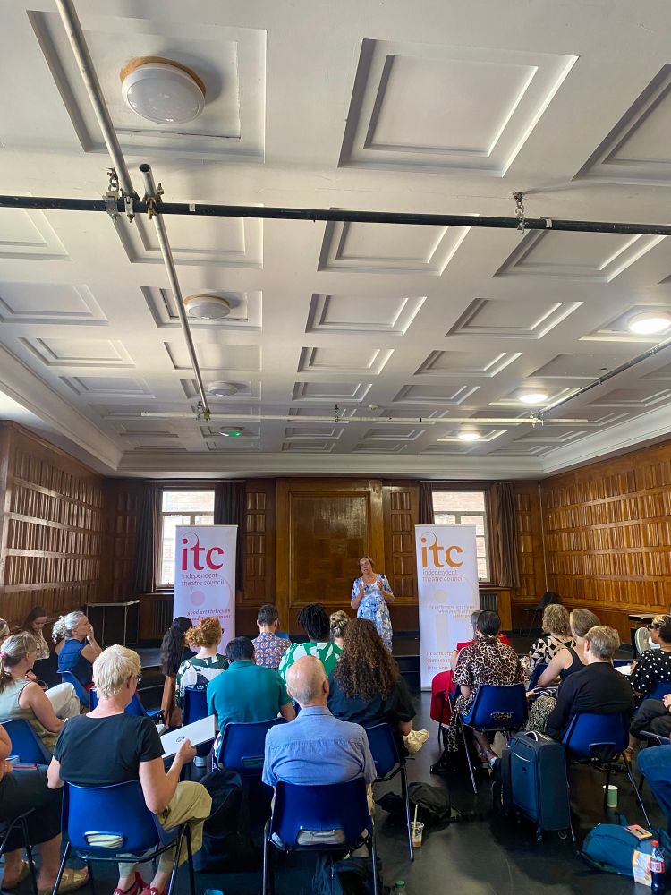 People sitting in a wooden panelled room with a presenter and ITC banners 