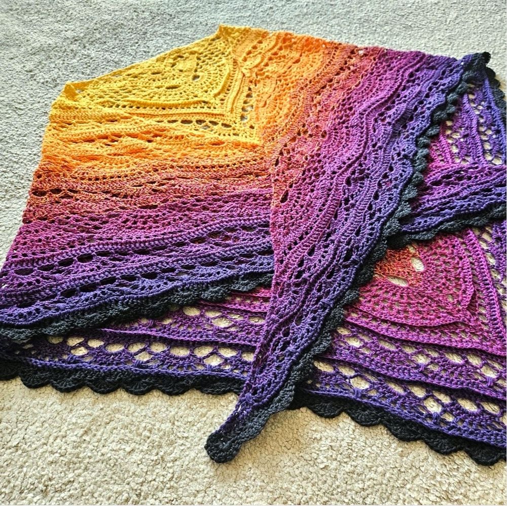 A crochet lace shawl in an orange to purple sunset gradient.
