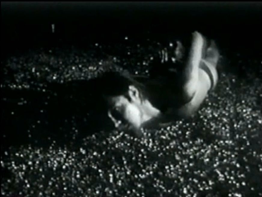 Chris Burden crawls on their stomach, wearing only briefs and with their hands held behind their back, through a parking lot covered with shattered glass. 