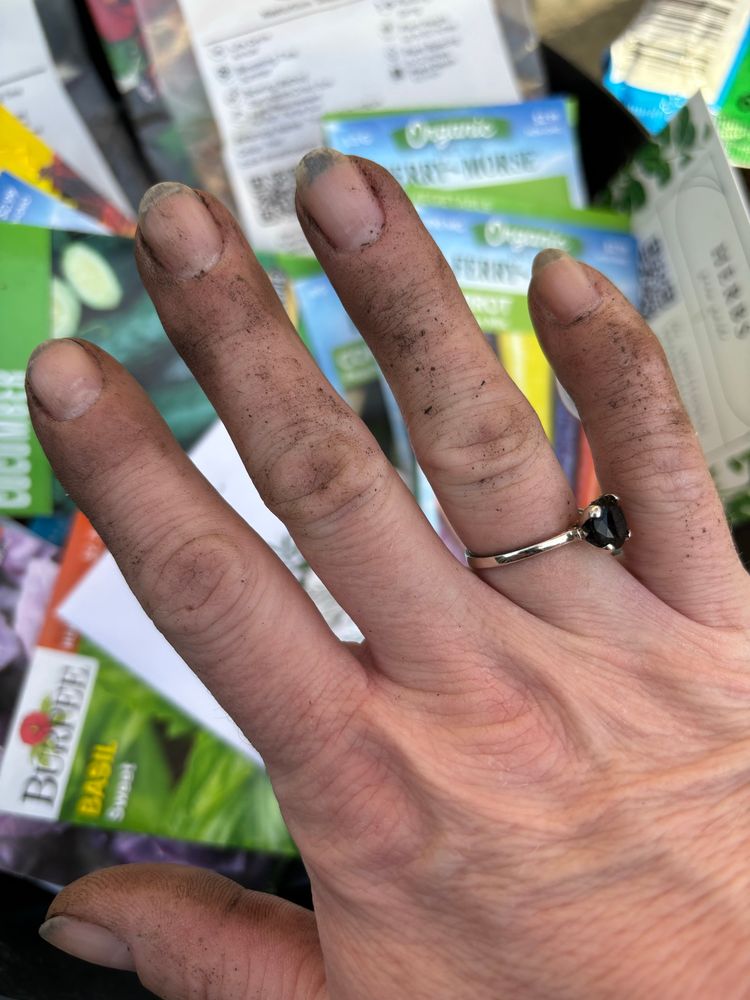 Dirt under fingernails, dirty hands, seed packets in the blurred background.