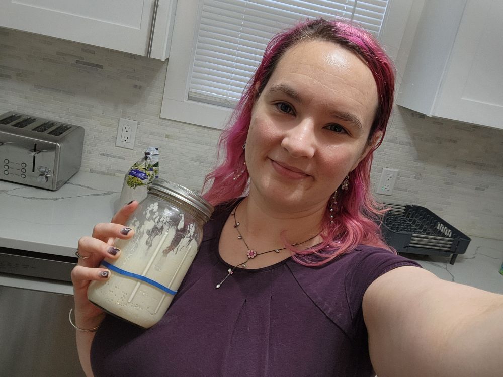A woman with pink hair holds up a jar of sourdough starter 