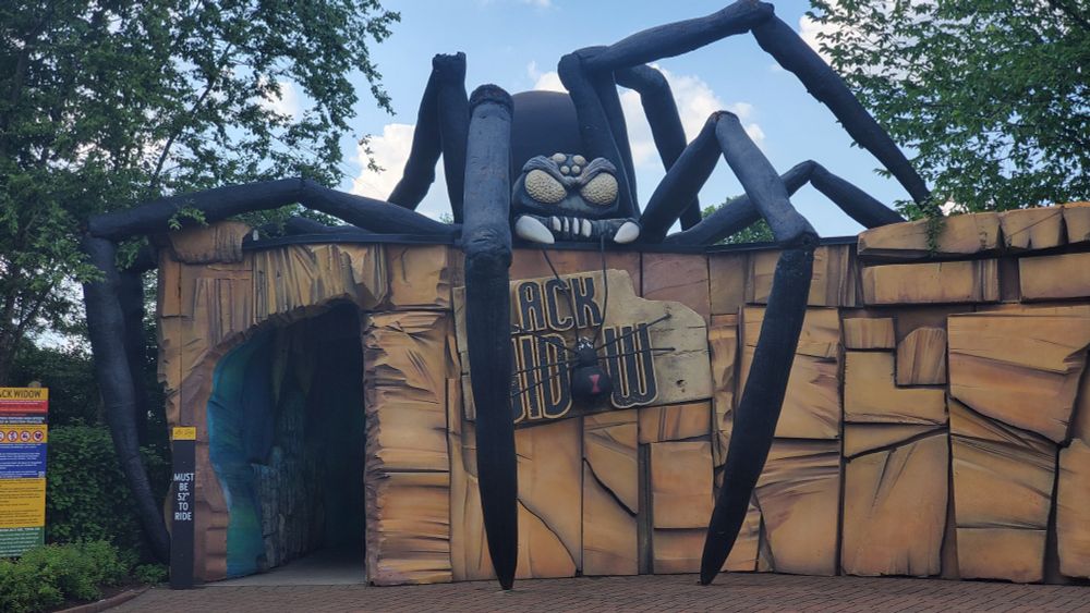 Entrance building of Black Widow pendulum ride at Kennywood featuring a large menacibg looking black spider atop a stone facade building.