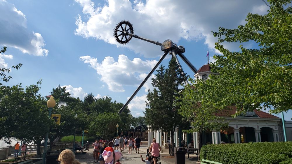Black Widow pendulum ride at Kennywood in the distance swinging at one of its apexes while looking down a midway walking toward it.