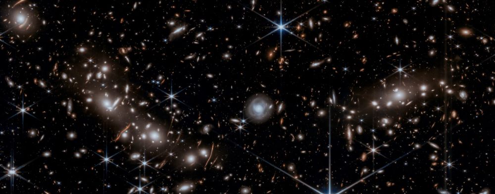 A deep-field image captured by the James Webb Space Telescope's NIRCam instrument, showcasing the aftermath of a colossal collision between two galaxy clusters. The image reveals a complex web of galaxies, gas, and dust, with the most prominent feature being a bridge of hot gas stretching between the two main clusters.