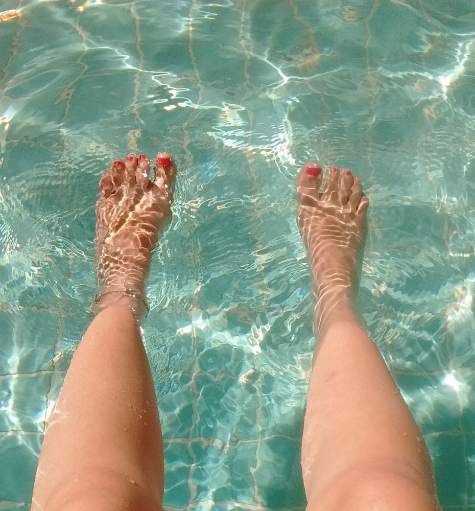 Olhando os próprios pés na água da piscina com raios de sol refletindo
