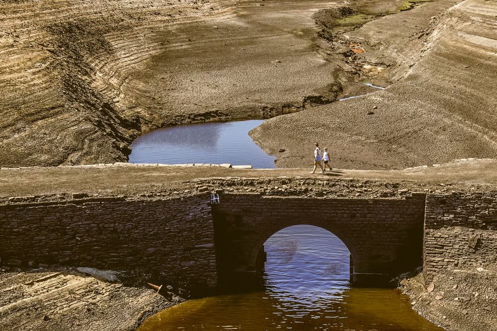 Two people walk across an arid bridge in a dried out river in Yorkshire.