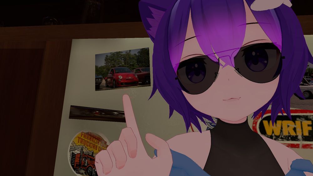 selfie of a vrchat anime gril pointing at a photograph of her IRL car on a minifridge