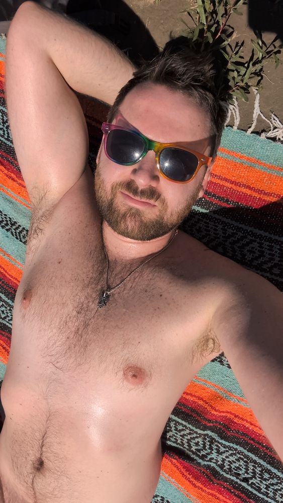 A picture of me laying on a blanket, showing my torso and my arm is raised with my hand underneath my head  I'm wearing only rainbow sungalsses