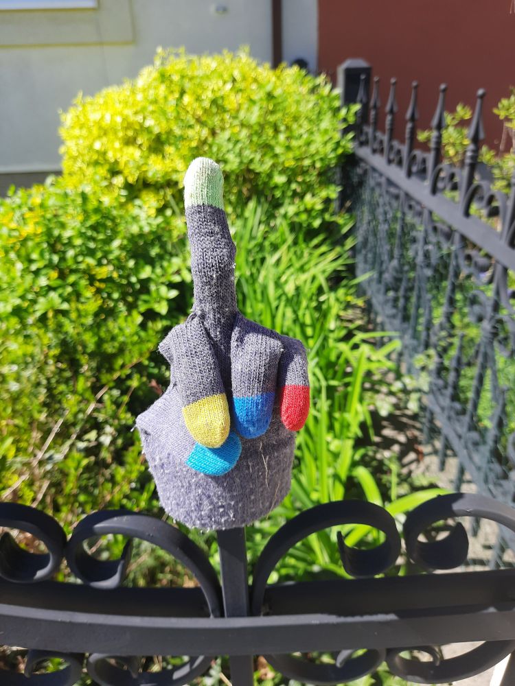 Rukavice na plotě se vztyčeným prostředníčkem.