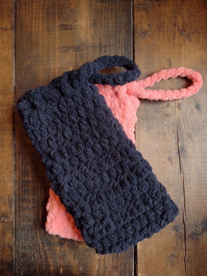 Two crochet drawstring phone pouches, one in black and one in coral