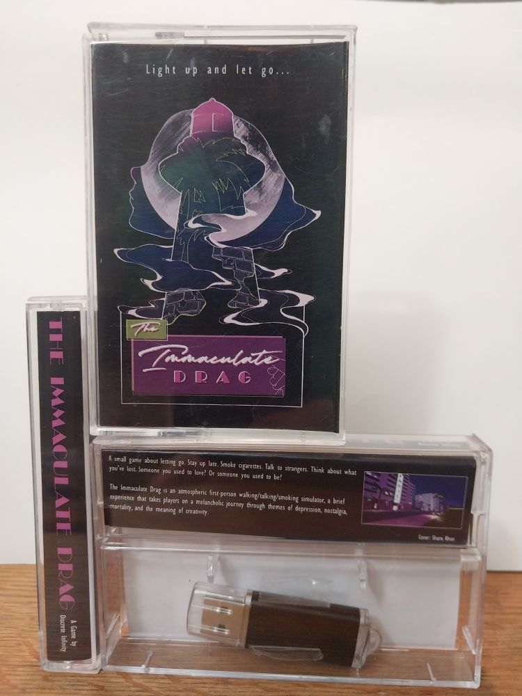 physical edition of the game "the immaculate drag" showing the front, back, and spine of a tape cassette case with USB stick inside