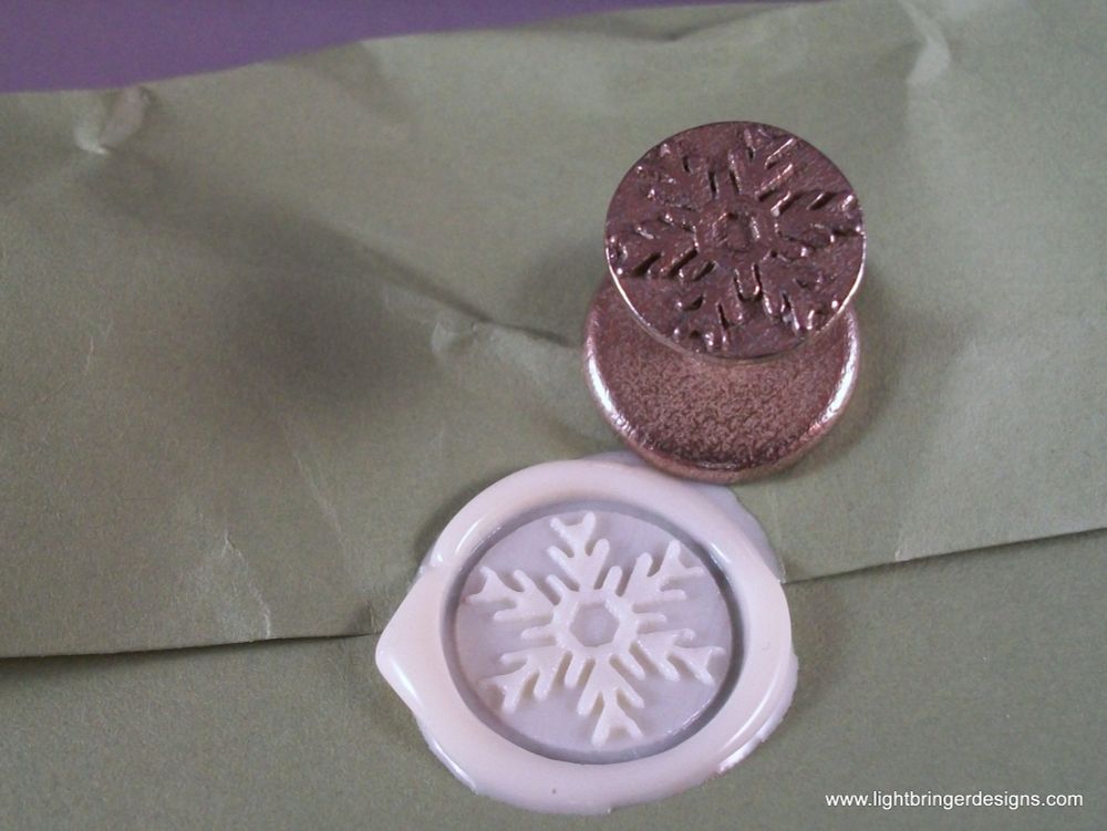 Photo of a snowflake wax seal in white wax, with branches angled differently so they change brightness with your perspective relative to the light, and the 3D printed stamp that makes it. 
The stamp also has the same design on top of the handle so it's easier to set straight. 