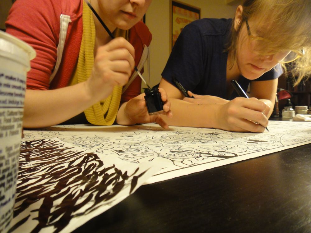 Erika and Lucy hunched over an illustration that they're both inking, 2013.