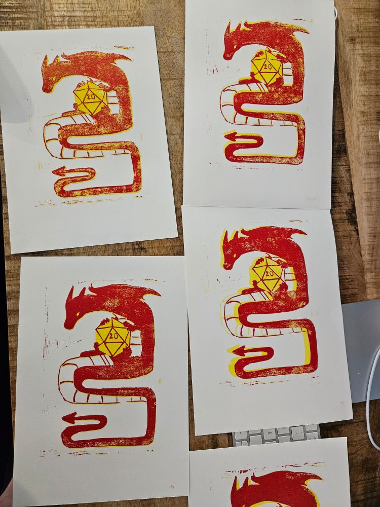 Four sheets of paper with a red dragon holding a yellow 20 sided die prinred onto them.