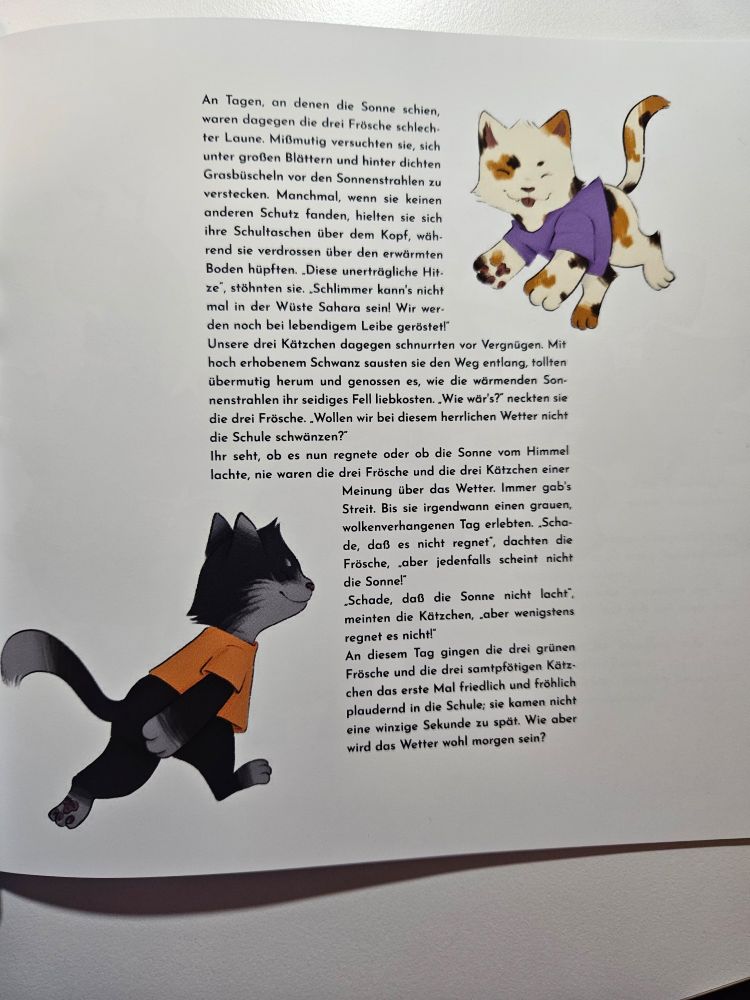 A page of a book.
Two illustrations of anthropomorphic kittens frame text in the center.
The kitten on the bottom left is black with light grey tuxedo markings and wearing an orange t-shirt.
The kitten on the top right has calico markings and is wearing a purple t-shirt.