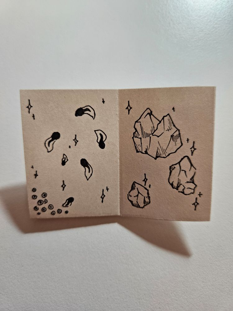 Another two page spread of the tiny zine.
The left page shows frog eggs in the bottom left corner and a total of six tadpoles on the rest of the page. They are surrounded by sparkles.
The right page shows three rough gemstones also surrounded by sparkles.