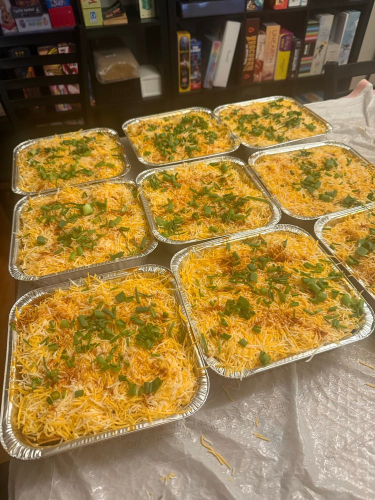 Nine 8”x8” foil pans full of enchiladas, covered in shredded cheese blend and garnished with smoked paprika and spring onions. 