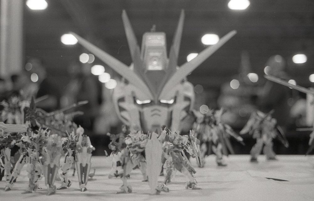 a bw photo of gunplas on a table; a large Gundam head looms in the bg