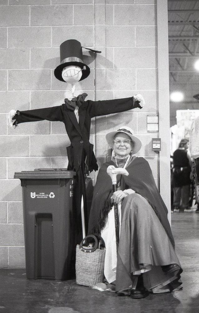 a photo of an older Sophie cosplay from Howls moving Castle. she has the scarecrow beside her as well.