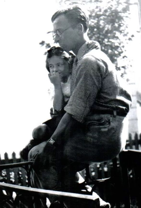 B&W 1930s photograph of a bespectacled man's profile from the side. His young daughter is sitting on his lap with her arm around his neck. We can't see what they're looking at.