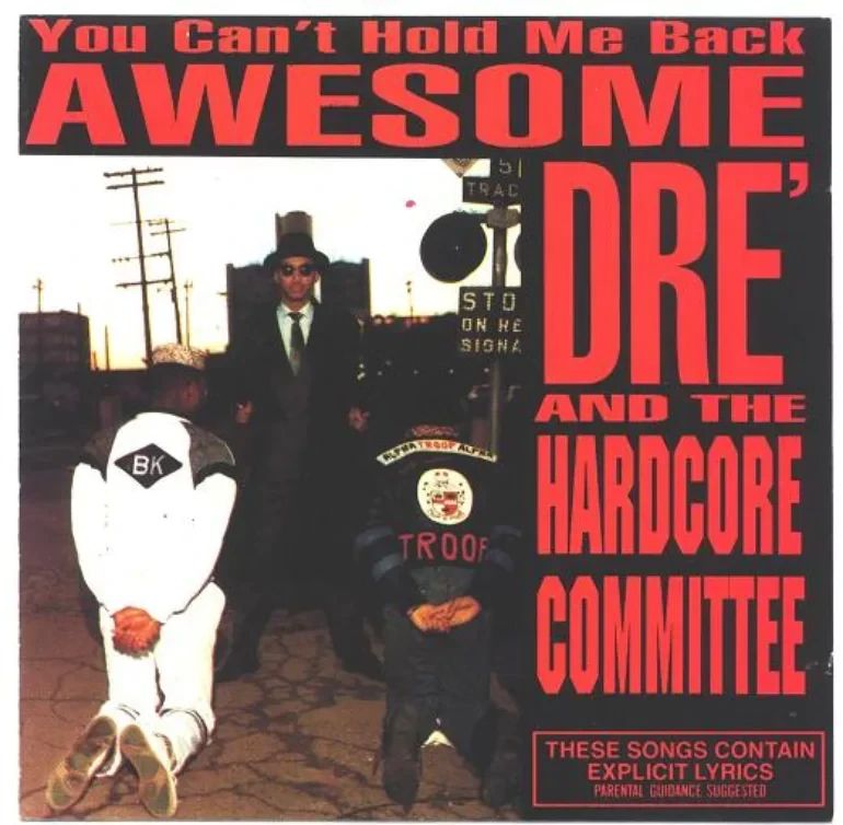 Album cover for You Can’t Hold Me Back by Awesome Dre and the Hardcore Committee. The photo shows a tense street scene: two young Black men in tracksuits kneel on the pavement with their hands behind their backs as if detained, one with “BK” on his jacket and the other with “TROOP.” Standing over them is a man in a dark suit, tie, and wide-brimmed hat, staring down with authority. Behind them, a stop sign and telephone poles set the urban backdrop. The cover text is bold and confrontational, with huge red letters reading AWESOME DRE’ AND THE HARDCORE COMMITTEE along with the album title You Can’t Hold Me Back. At the bottom right, a warning box notes: These songs contain explicit lyrics. Parental guidance suggested. The imagery underscores themes of resistance, systemic oppression, and defiance.