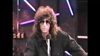 a video still of howard stern seated at a microphone from his early 1990’s channel 9 TV show