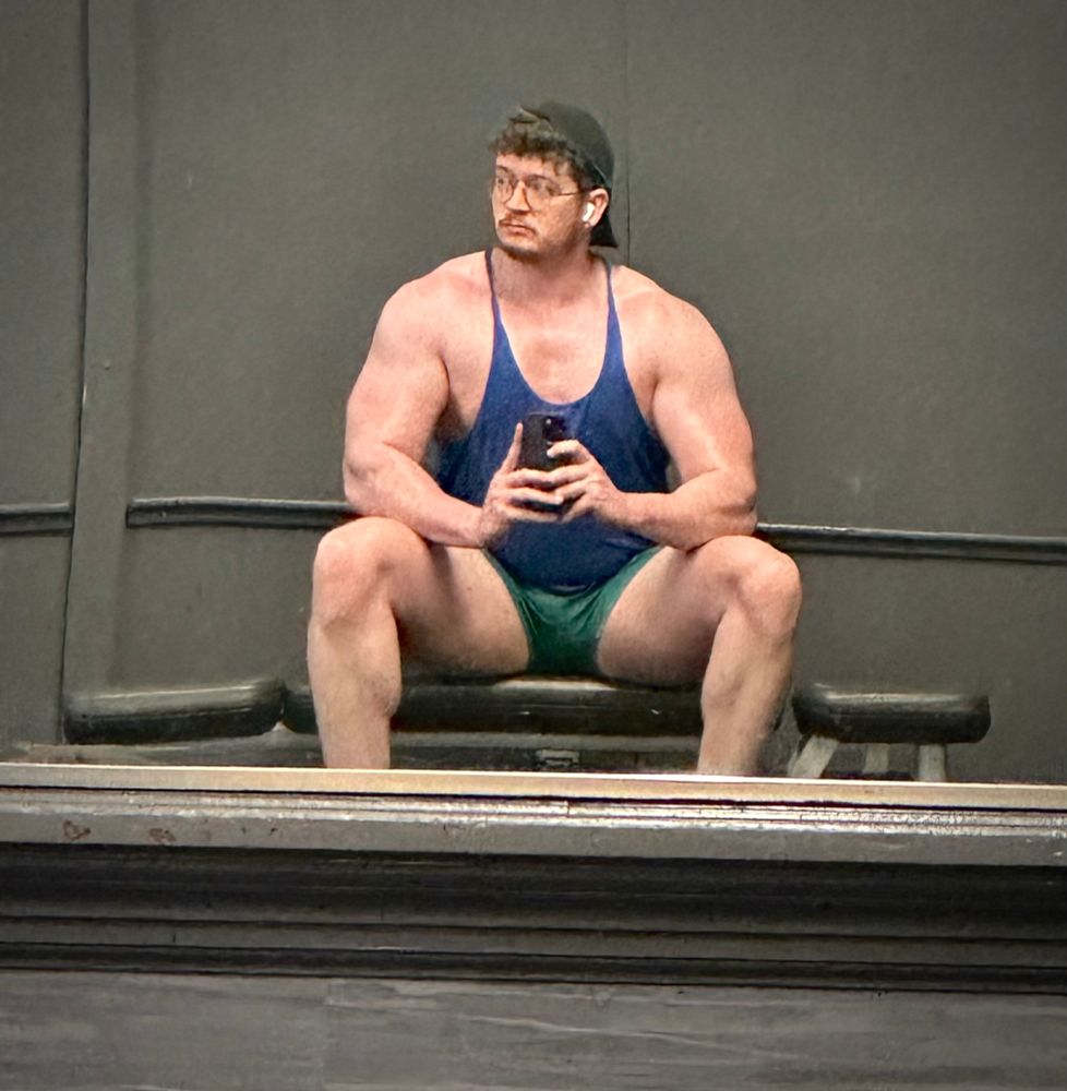 Man in blue tank top seated on a gym bench. 