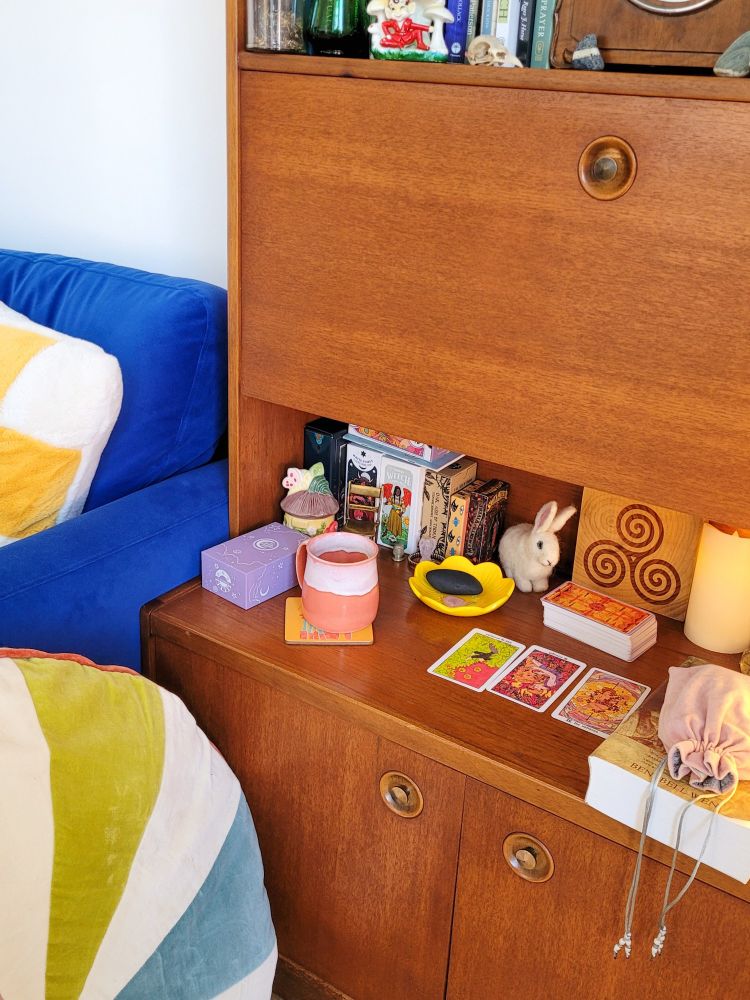 an altar with various items on it, including a mug of tea and tarot cards spread out.