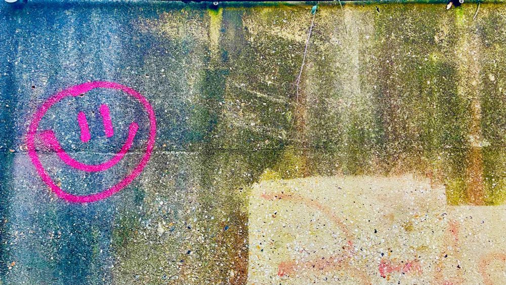 A wall with a bright pink smiley face spray-painted on