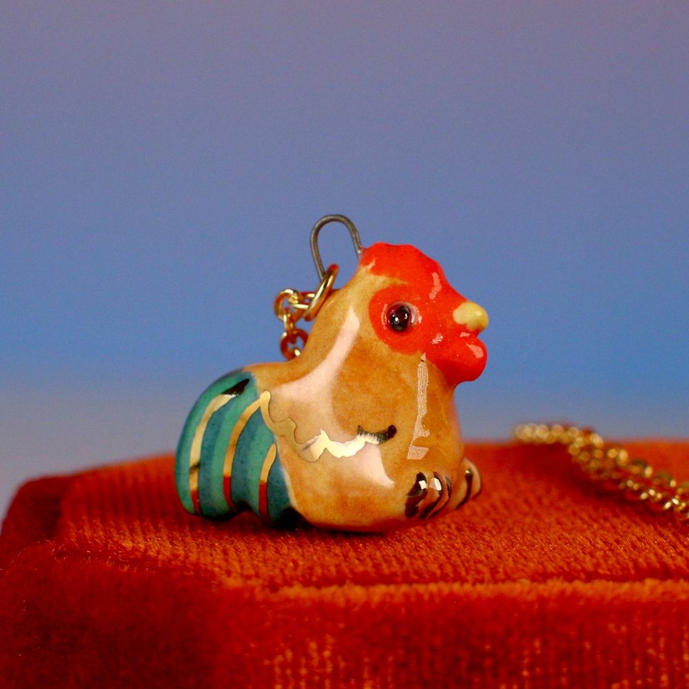 Ceramic chonky rooster pendant. Tan body, green tail feathers & gold details. 