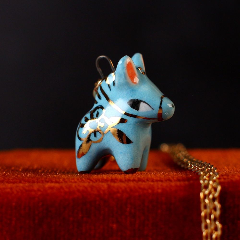 Blue ceramic horse charm with painted gold floral details. 