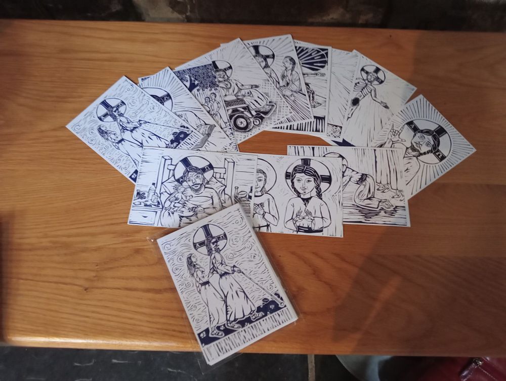 An array of postcards featuring lino print images of Disabled Christ fanned out on a wooden bench