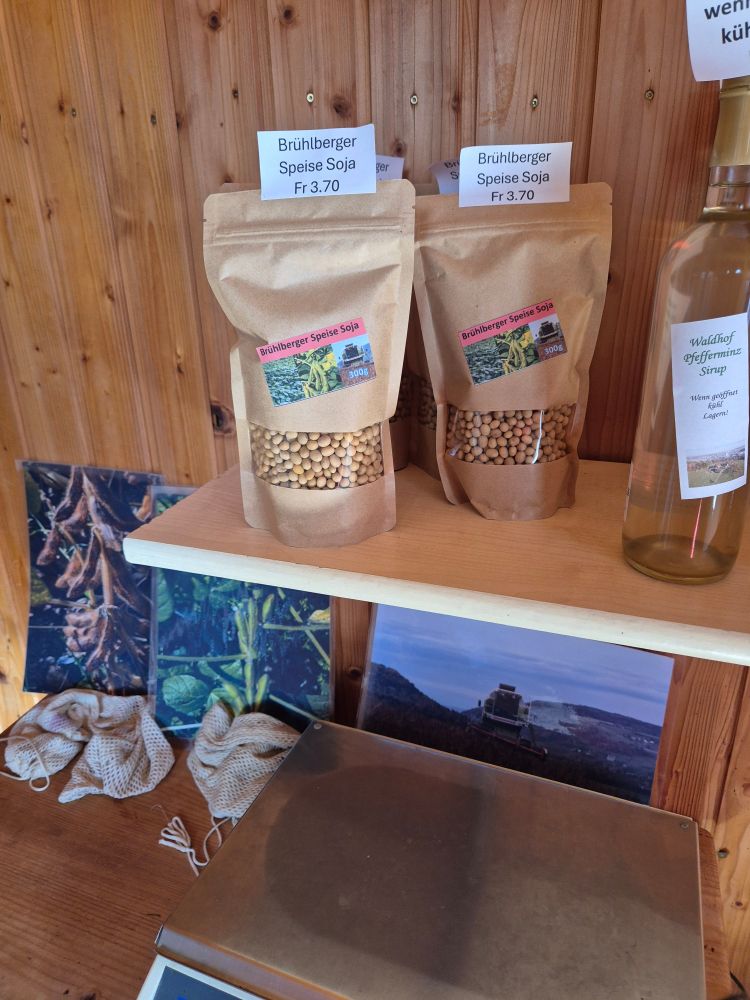 Bags of soy beans for sale on a shelf. Below the shelf are photos of the soy plants and a scale. Also, at the edge some wonderful peppermint syrup which I bought, along with free range eggs (from hens also foddered from the farm's own products).
I don't do raw milk, even here, or I'd buy that too from their coin opperated self service tank next door to this cupboard sized honestly box shop.