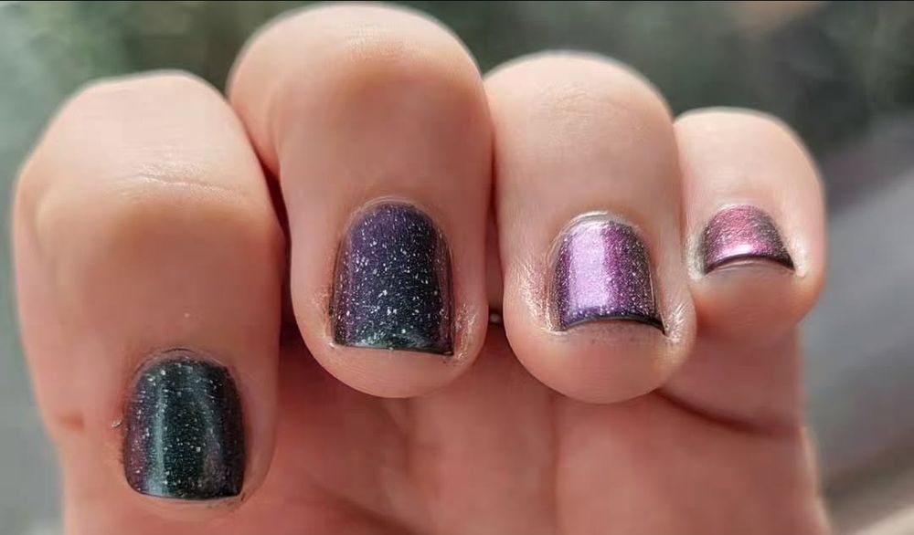 Close up of fingernails displaying a color shifty glittery nail polish going from deep teal through blue to purple.