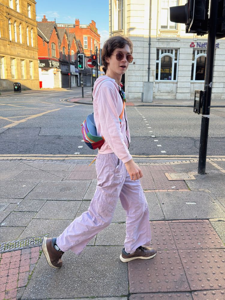 felix in a lavender-pink fit mid-stride on a pavement looking at the camera in sunglasses. it is sunny and daytime early morning