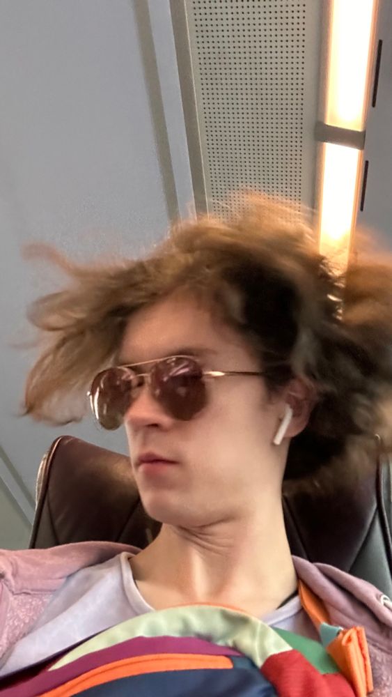 a person (me) with sunglasses and airpods sat on a bus shaking my hair so it puffs out