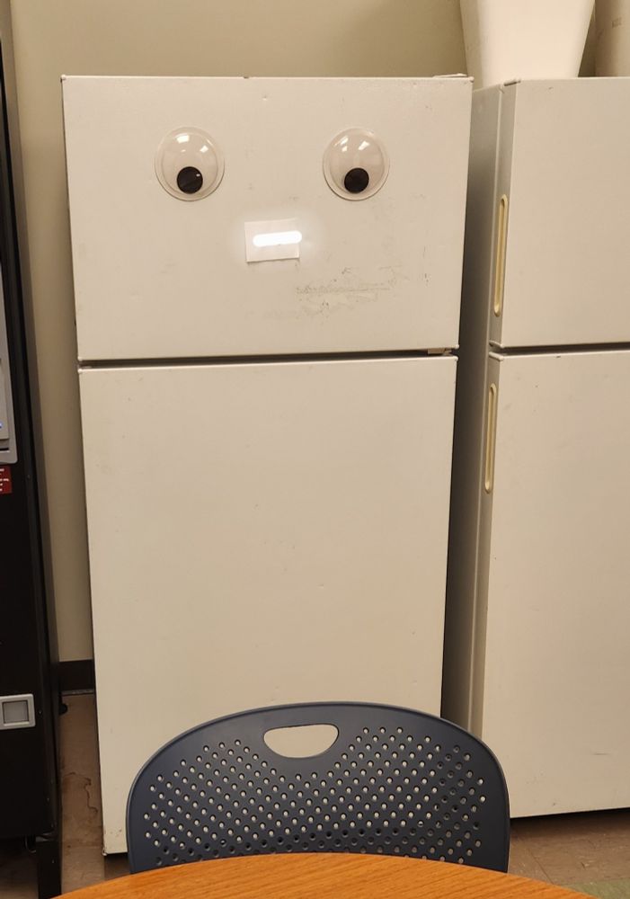 A work refrigerator with huge googly eyes on the front. The fridge looks friendly.