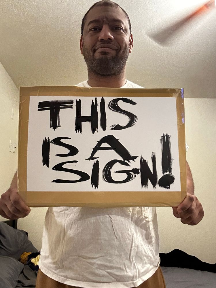 A man holding a sign reading “this is a sign”.